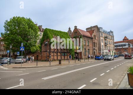 Vue sur la rue à Gdansk, Pologne, avec une maison historique couverte de lierre avec une architecture traditionnelle en briques et en bois le long d'une route animée. Banque D'Images