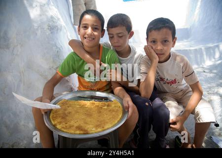 Chefchaouen, Maroc, le 3 juillet 2007, trois enfants sont heureux de présenter leurs gâteaux faits maison en vente à Chefchaouen, mettant en valeur l’entrepreneuriat local Banque D'Images