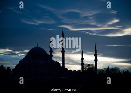 Silhouette de la mosquée Süleymaniye Istanbul Turquie // ISTANBUL, Turquie — les nuages de Wispy attrapent la lumière argentée du crépuscule derrière la silhouette de la mosquée Süleymaniye. La mosquée impériale ottomane du XVIe siècle, conçue par l'architecte Mimar Sinan, se trouve bien en vue sur la troisième colline d'Istanbul. Quatre minarets et le grand dôme central créent le profil distinctif de la mosquée face au ciel du soir. Banque D'Images