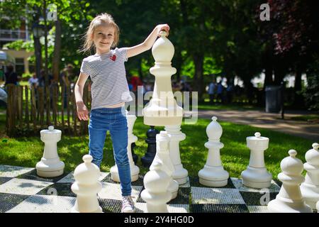 Adorable fille d'âge préscolaire jouant aux échecs avec de grandes pièces d'échecs à l'extérieur sur une journée d'été ensoleillée Banque D'Images