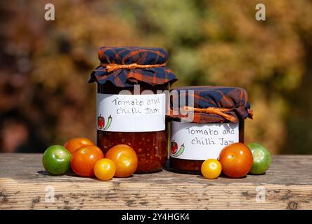 Royaume-Uni. Confiture ou chutney de tomates et de piments maison stockés dans des bocaux en verre, étiquetés et finis avec un topper en tissu. Une conserves de fruits de saison Banque D'Images