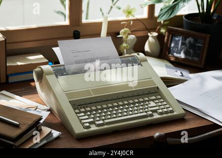 Lumière du soleil éclairant machine à écrire vintage sur un bureau en bois entouré de papiers, livres et plantes, créant une atmosphère nostalgique dans un espace de travail confortable Banque D'Images