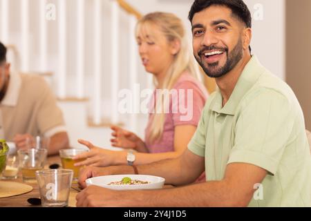 Homme souriant appréciant le repas avec divers amis à la table à manger, ayant du bon temps Banque D'Images