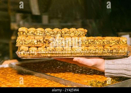 Main tenant un délicieux dessert, baklava sur un plateau, pâtisserie traditionnelle dans une boulangerie, concept de gâterie sucrée Banque D'Images