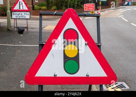 Panneau de signalisation britannique indiquant les feux de circulation devant un triangle d'avertissement rouge et blanc Banque D'Images