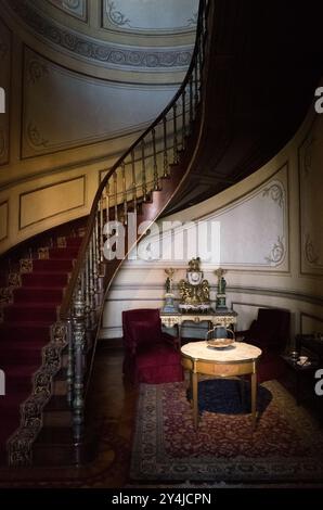 Quartiers résidentiels intérieurs du Château de Chapultepec, Mexico City | MEXICO CITY, Mexique — Un grand escalier en bois avec des balustres en métal ornés s'élève depuis un salon néoclassique situé dans les quartiers résidentiels du Château de Chapultepec. L'empereur Maximilien Ier et l'impératrice Charlotte ont profondément remodelé la structure vicéroyale d'origine de 1785 pendant le Second Empire mexicain (1864-1867), introduisant l'esthétique palatiale européenne dans les intérieurs. L'horloge de cheminée dorée, les garnissages en velours et les panneaux muraux délicats illustrent les normes de conception opulentes du XIXe siècle maintenues par les dirigeants ultérieurs, en Banque D'Images
