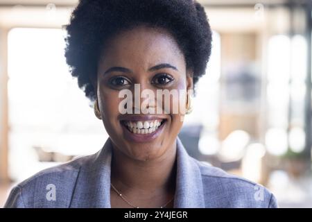 Femme d'affaires souriante au bureau portant blazer, regardant avec confiance la caméra Banque D'Images