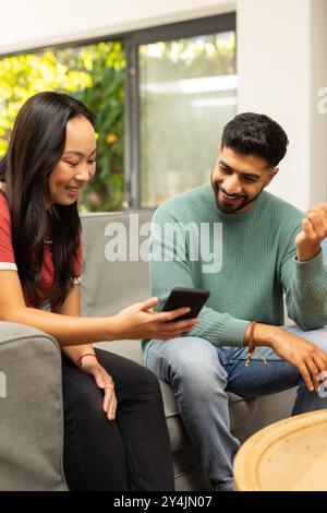 Souriant divers amis assis sur le canapé, regardant le smartphone et discutant ensemble Banque D'Images