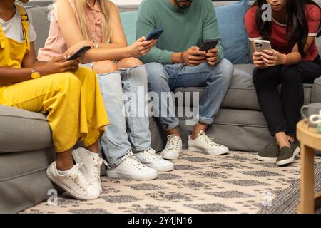 Assis sur le canapé, groupe d'amis utilisant des smartphones, se concentrant sur les écrans Banque D'Images