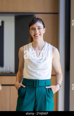 Souriante au bureau, femme d'affaires portant un chemisier blanc et un pantalon vert, les mains dans les poches Banque D'Images