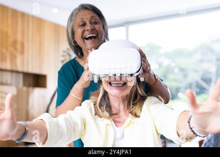 À la maison, en utilisant un casque vr, des amies féminines multiraciales seniors appréciant l'expérience de réalité virtuelle Banque D'Images
