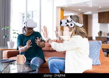 À la maison, en utilisant des casques vr, deux amies féminines multiraciales seniors interagissant et s'amusant Banque D'Images