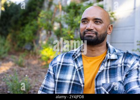 Homme souriant dans la chemise à carreaux appréciant le temps extérieur dans le jardin de la maison Banque D'Images