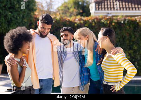Groupe de jeunes amis divers debout ensemble à l'extérieur, souriant et s'embrassant les uns les autres Banque D'Images