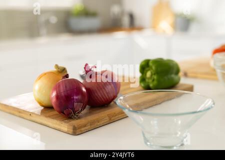 Hacher des oignons et du poivron sur une planche à découper en bois dans une cuisine moderne Banque D'Images