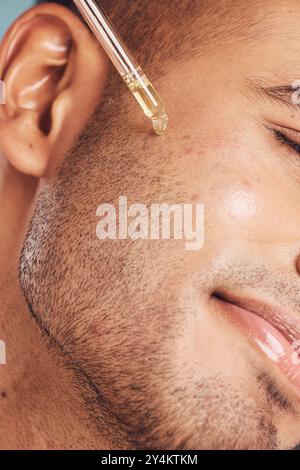 Soins de la peau, visage et homme avec sérum en pipette, produit de traitement de l'acné ou éclat de la peau sur fond bleu. Cosmétiques, goutte de rétinol et personne masculine avec de l'huile Banque D'Images