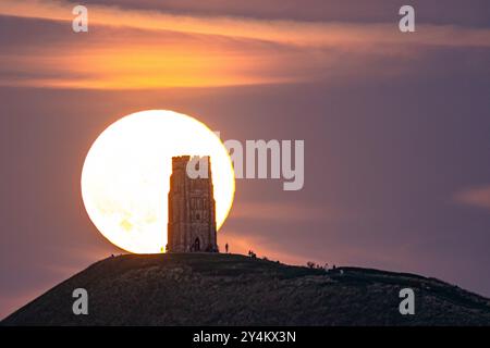 Les gens se rassemblent alors que la super lune se lève au-dessus de la tour St Michael, au sommet de Glastonbury Tor, qui se produit lorsque la lune apparaît 30% plus lumineuse et 14% plus grande dans le ciel. Date de la photo : mercredi 18 septembre 2024. Banque D'Images