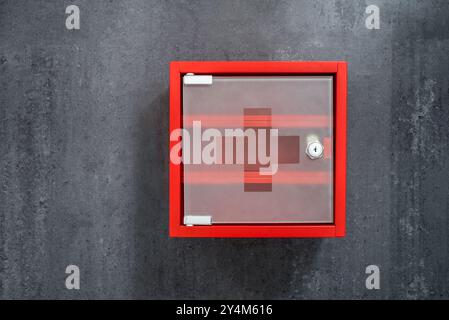 Armoire de médecine vide en métal rouge fermé suspendue sur Un fond de mur en marbre gris foncé. Vue de face Banque D'Images