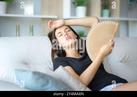 Femme stressée assise sur un canapé à la maison ventilant une chaude journée d'été Banque D'Images