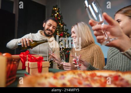 Des amis portent un toast avec du vin mousseux lors d'un dîner de Noël à la maison. Banque D'Images