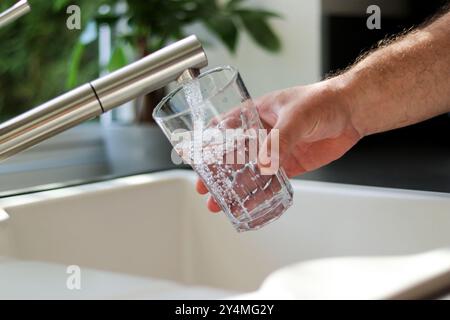 Gros plan de mains masculines versant de l'eau du robinet dans un verre dans la cuisine Banque D'Images