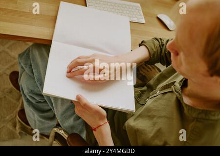 Plan haut en bas d'un homme méconnaissable avec une déficience visuelle assis à une table en bois et lisant un livre en braille Banque D'Images