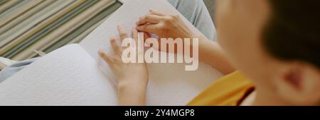 Plan haut vers le bas d'une femme méconnaissable appréciant la lecture du livre braille à la maison Banque D'Images