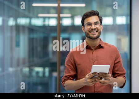 Homme d'affaires souriant tenant la tablette dans le cadre de bureau transmet la confiance et l'engagement avec la technologie. L'environnement professionnel met en évidence la dynamique et le succès du lieu de travail moderne. Banque D'Images