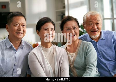 deux heureux couples asiatiques âgés assis sur le canapé à la maison regardant la télévision ensemble Banque D'Images