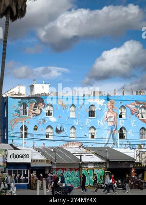 Venice Beach, États-Unis - 31 mars 2024 : personnages accidentels devant Venice Kinesis Street art murale par Rip Cronk contre le ciel bleu avec des nuages Banque D'Images