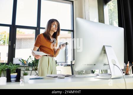 Une jeune personne non binaire équilibre la paperasse et un téléphone, engagée dans un travail de bureau productif. Banque D'Images