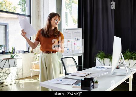 Engagé dans le travail, un jeune individu non binaire équilibre la paperasse et la technologie dans un bureau moderne. Banque D'Images