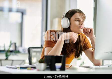 Engagé dans la pensée profonde, une jeune personne non binaire est assise à leur bureau, occupé par des tâches de travail. Banque D'Images