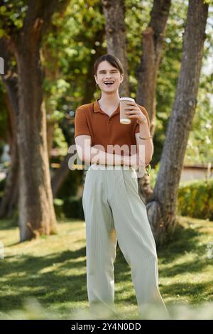 Un jeune individu non binaire sirote joyeusement une boisson dans un jardin de bureau animé. Banque D'Images