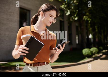 La jeune personne non binaire se tient dehors, concentrée sur son téléphone, café à la main. Banque D'Images