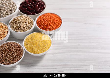 Différents types de céréales et de légumineuses dans des bols sur une table en bois blanc. Espace pour le texte Banque D'Images