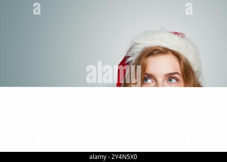 Femme de Noël dans le chapeau de Père Noël tenant le placard blanc vide de panneau de bannière avec l'espace de copie Banque D'Images