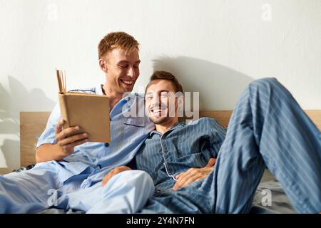 Un joyeux couple gay partage un moment chaleureux, lisant et riant ensemble dans leur pyjama douillet. Banque D'Images