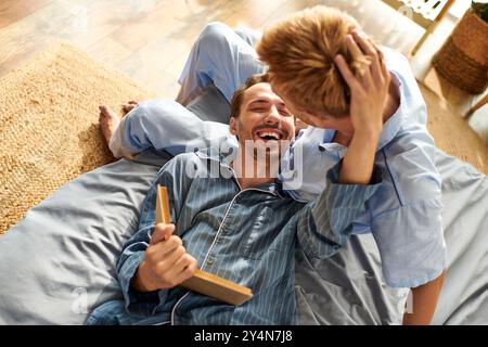 Un couple gay aimant profite d’une matinée joyeuse ensemble, partageant rire et chaleur dans leur pyjama. Banque D'Images