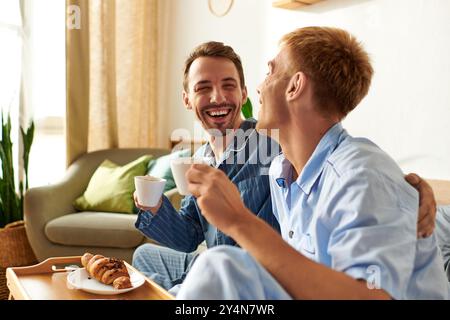 Un joyeux couple gay profite d'une matinée chaude ensemble, partageant sourires et boissons dans leur confortable pyjama. Banque D'Images