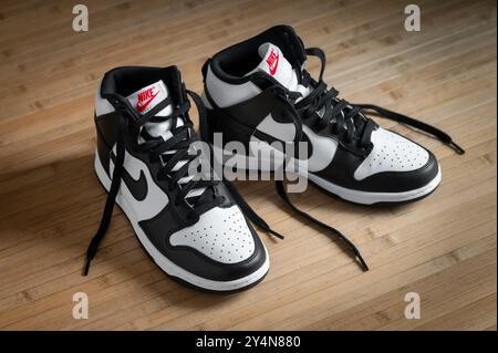 Nouvelles sneakers nike dunk high panda sur un sol en bois franc élégant, avec logo Swoosh emblématique en cuir noir et blanc. Parfait pour l'extérieur décontracté ou sportif Banque D'Images