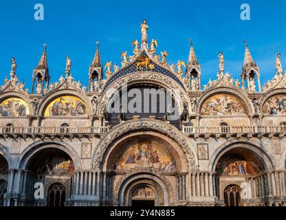 Cathédrale Basilique de Saint Marc façade de l'église avec entrée brillante dans la lumière du soleil du soir à Venise Italie Europe contre ciel bleu sans nuages Banque D'Images