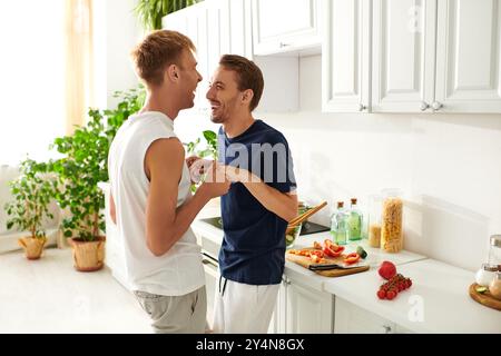 Deux hommes hachent joyeusement des légumes et préparent une salade ensemble dans leur cuisine moderne et lumineuse. Banque D'Images