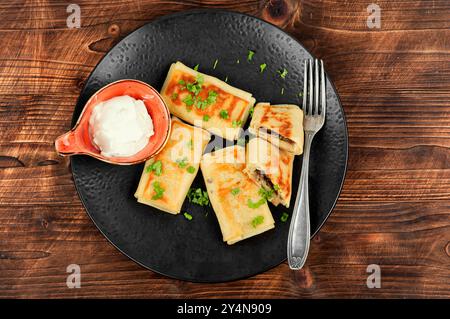 Crêpes farcies de foie de bœuf et de crème sure sur une assiette. Crêpes pour le petit déjeuner sur une table en bois rustique. Banque D'Images