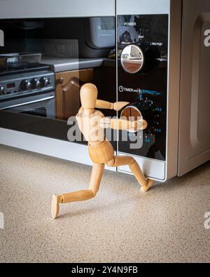 Mannequin en bois utilisant un four à micro-ondes. Utilisation de l'appareil de cuisine, cuisson, réglage du concept de minuterie micro-ondes Banque D'Images