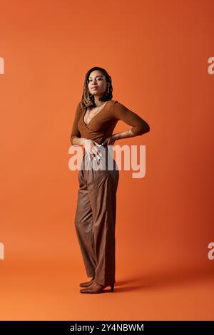 Une jeune femme à la mode présente son style avec des cheveux tressés, frappant une pose dans un décor de studio dynamique. Banque D'Images