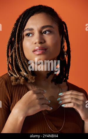 Une jeune femme met en valeur ses cheveux tressés et son style unique tout en posant dans un environnement de studio lumineux. Banque D'Images