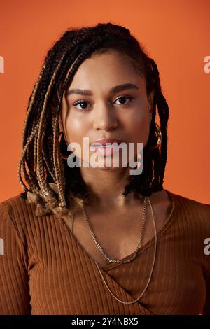 Une jeune femme afro-américaine respire la confiance et le style, mettant en valeur ses cheveux tressés sur une toile de fond audacieuse. Banque D'Images