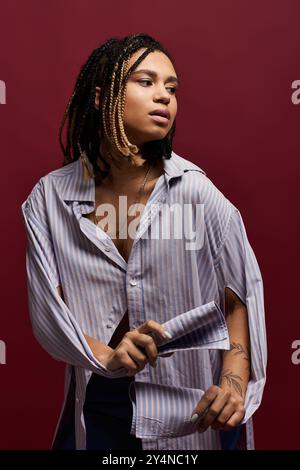 Une jeune femme à la mode avec des cheveux tressés met en valeur son style dans un fond audacieux, exsudant confiance et flair. Banque D'Images