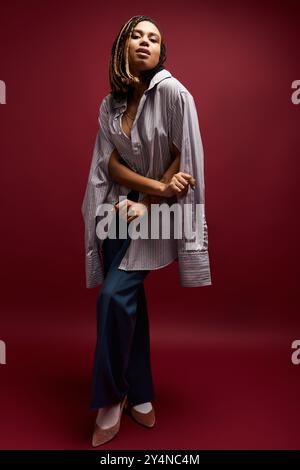 Une jeune femme afro-américaine met en valeur son style avec des cheveux tressés et une tenue chic dans un décor studio dynamique. Banque D'Images